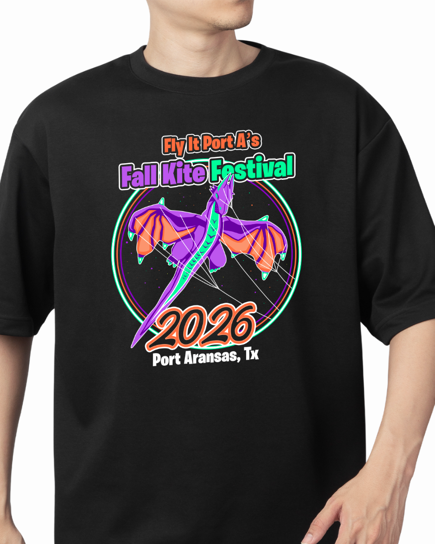 A man wearing a black t-shirt with a colorful graphic print for 'Fly It Port A's Fall Kite Festival 2026 Port Aransas, Tx'. The graphic features a purple and orange dragon kite design with a green outline.