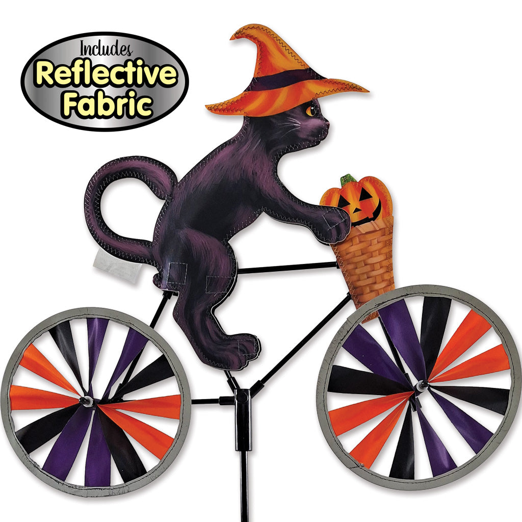 Halloween yard sign featuring a black cat riding a bicycle with orange, purple, and black striped wheels, wearing an orange witch hat, with a pumpkin basket on the handlebar. Includes reflective fabric.