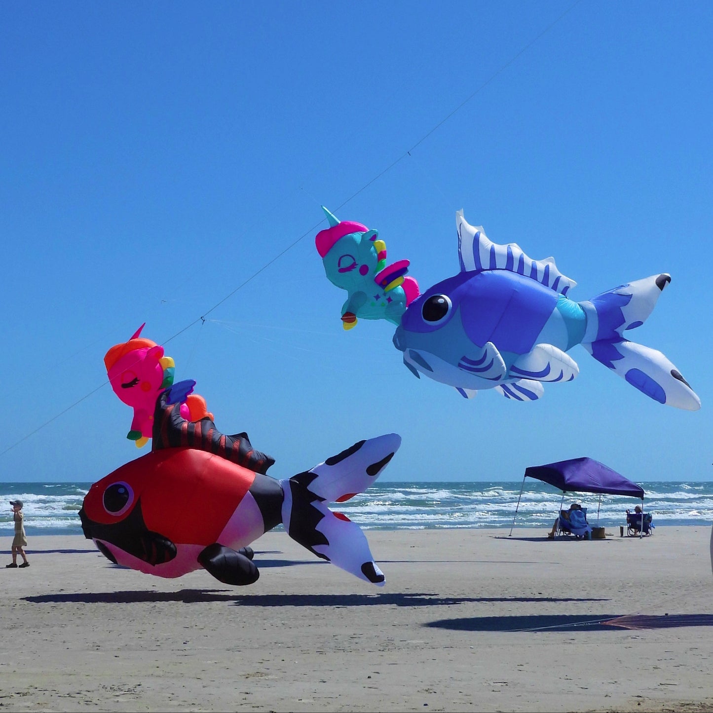 Colorful inflatable fish kites flying over a beach with a clear blue sky.