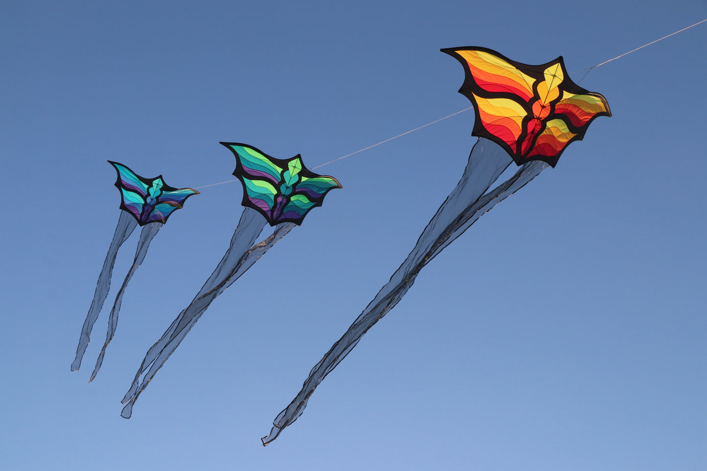 Three colorful kites flying against a clear blue sky.