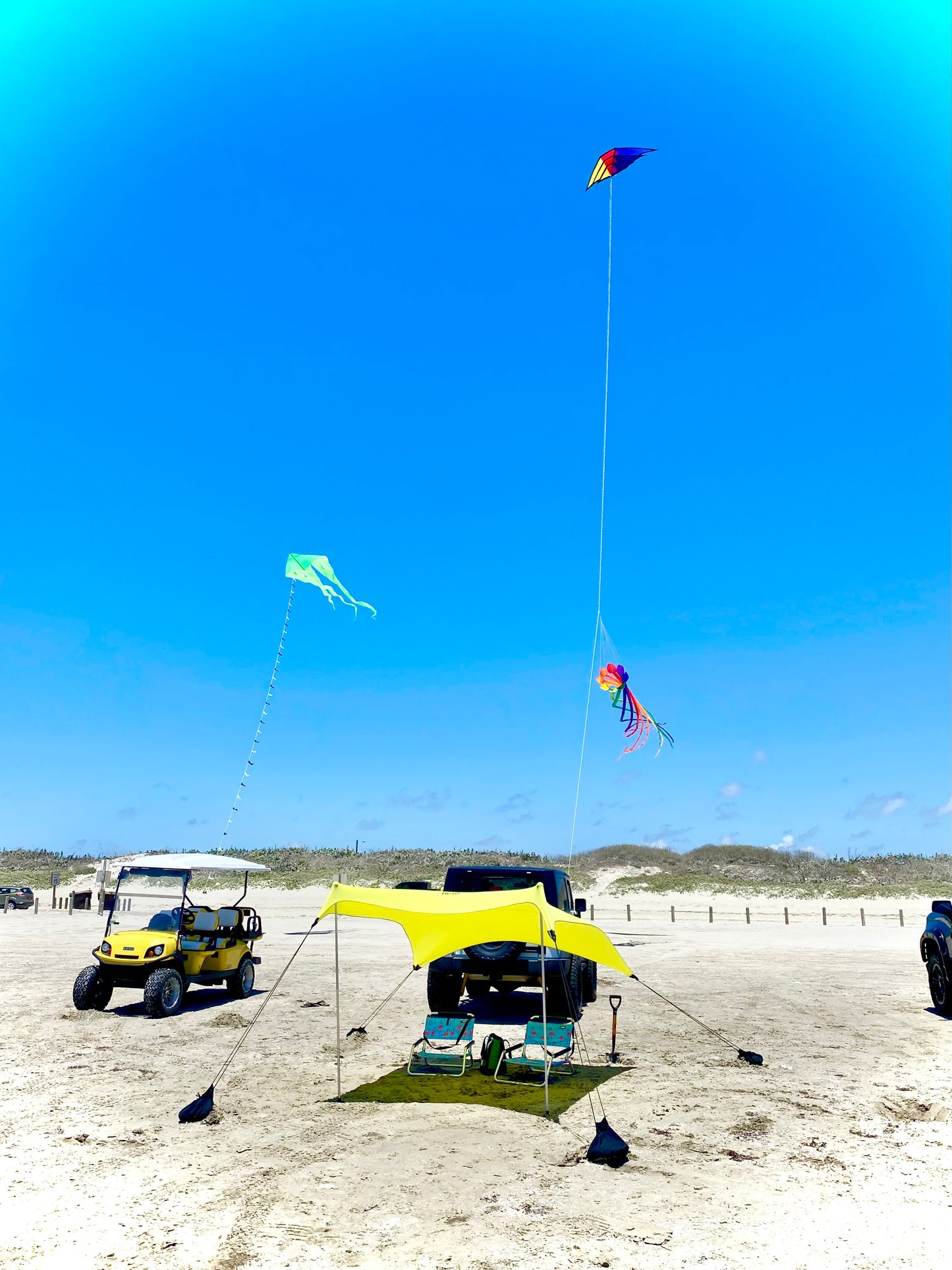 Beach scene with a yellow canopy, kites flying, and beach vehicles.