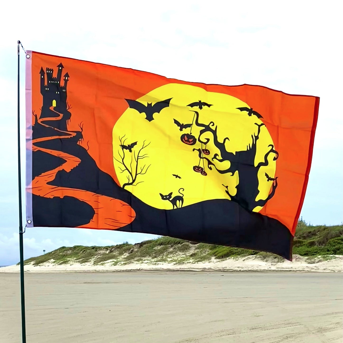Halloween-themed flag with a full moon, bats, and pumpkins on a beach.