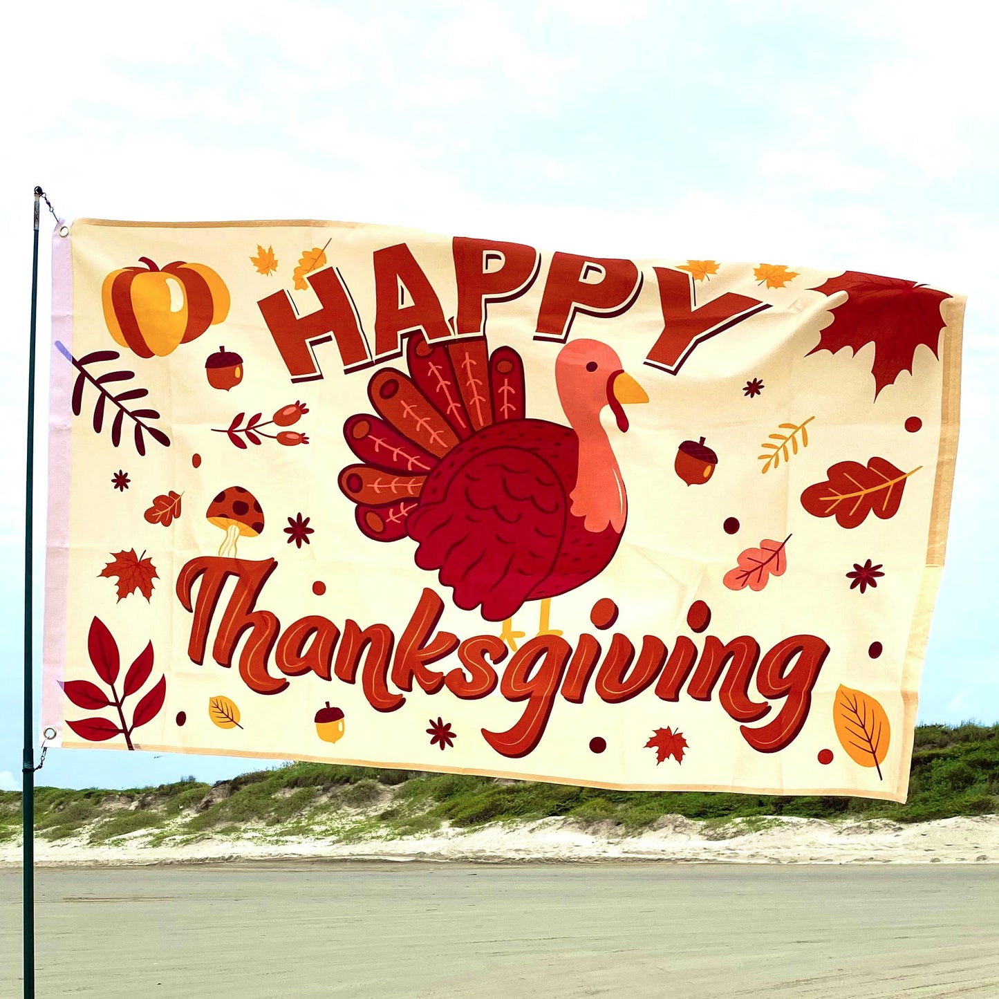 Thanksgiving-themed flag with a turkey and autumn elements on a beach.