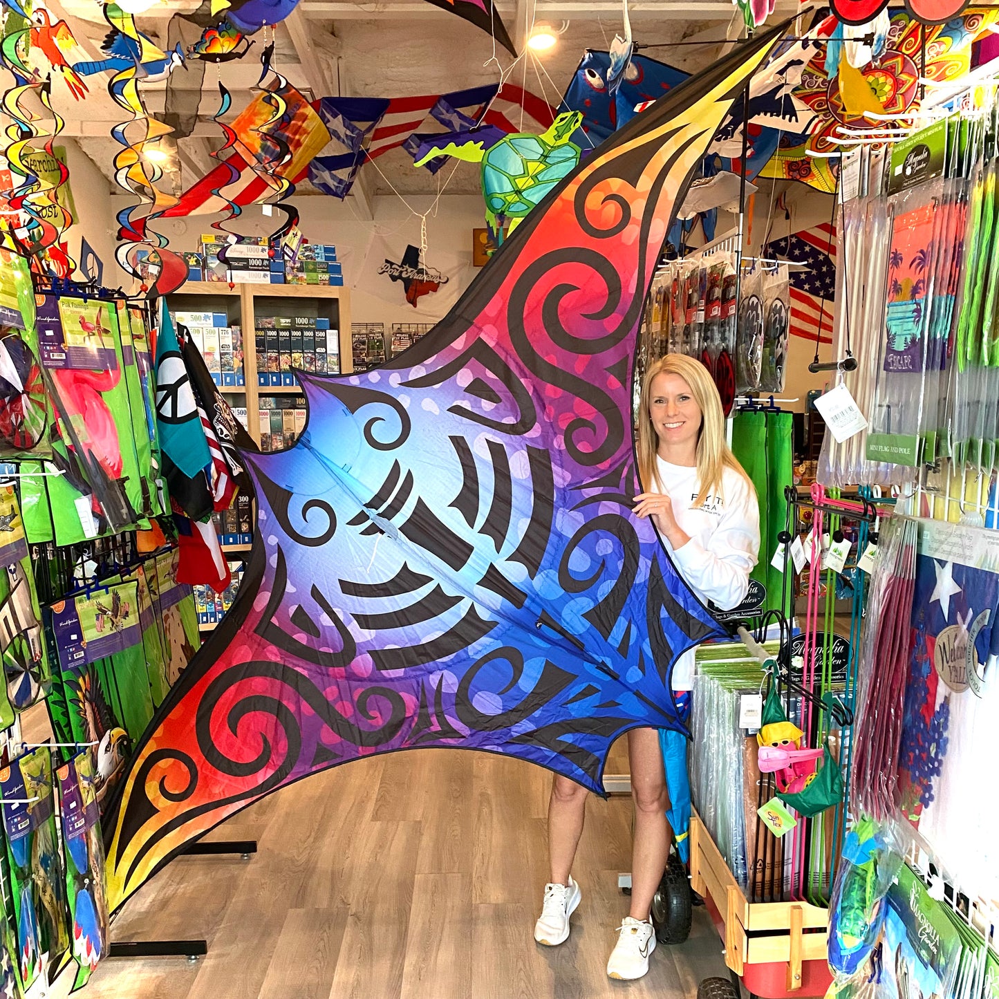 Woman holding a large, colorful kite in a store filled with various kites and products.