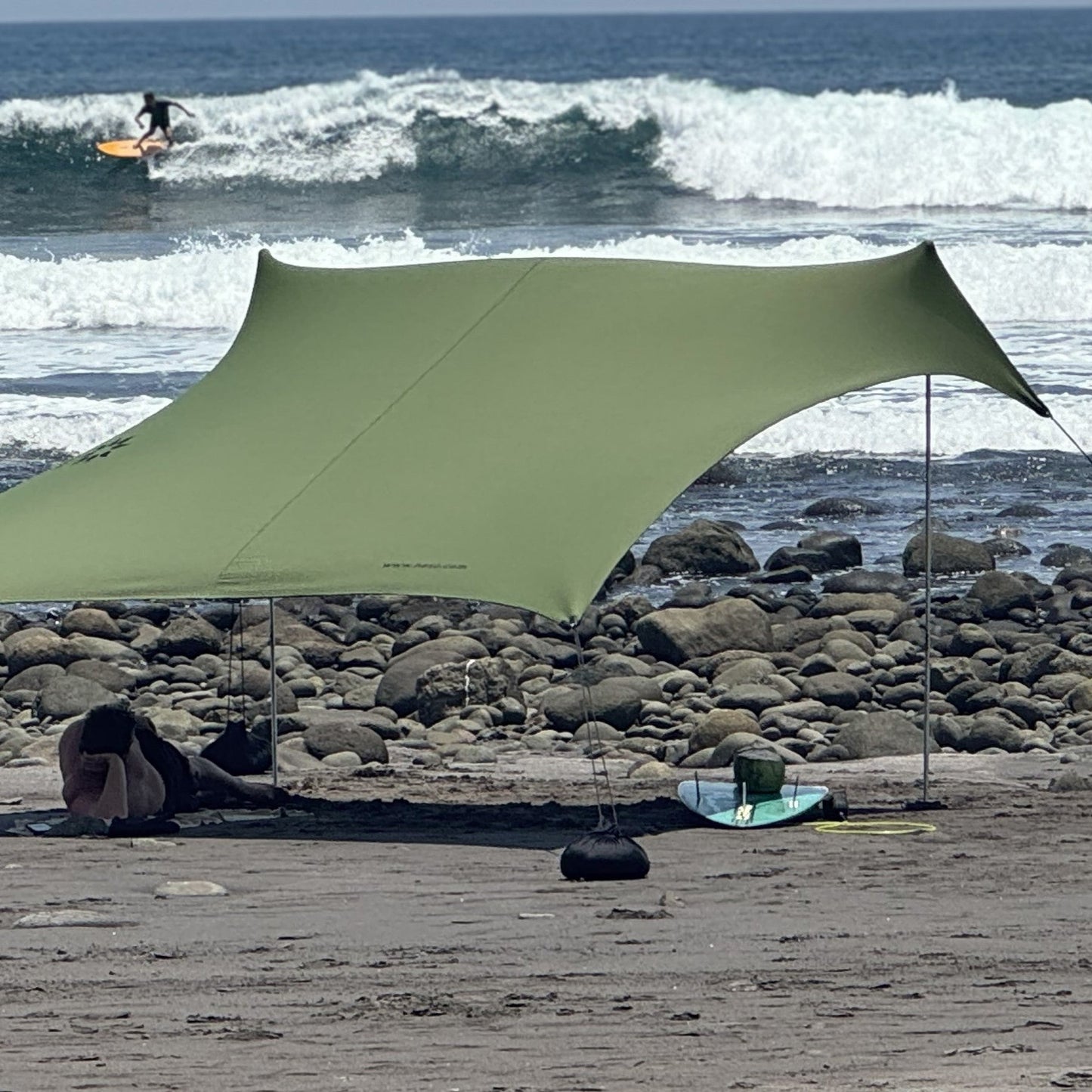 Green canopy set up on a rocky beach with ocean waves in the background