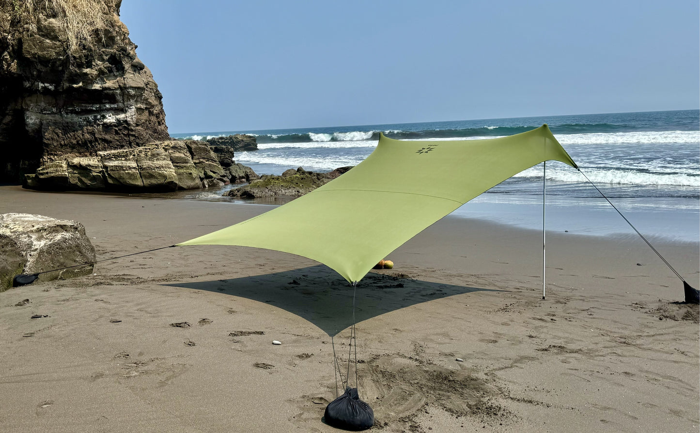 Green canopy set up on a sandy beach with ocean waves in the background