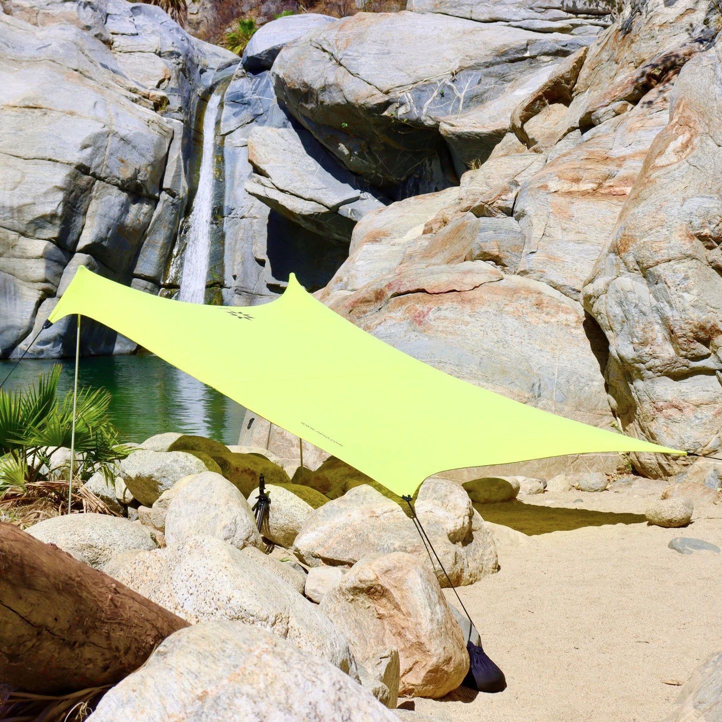 Yellow NESO tent set up on a rocky beach with water and rocks in the background
