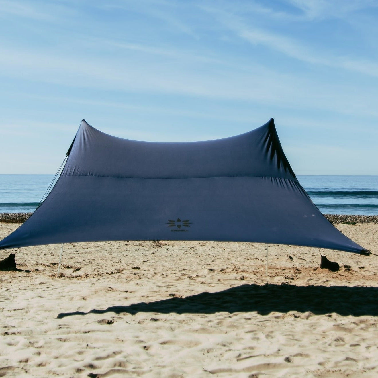 Navy NESO beach shade on a sandy beach with ocean in the background