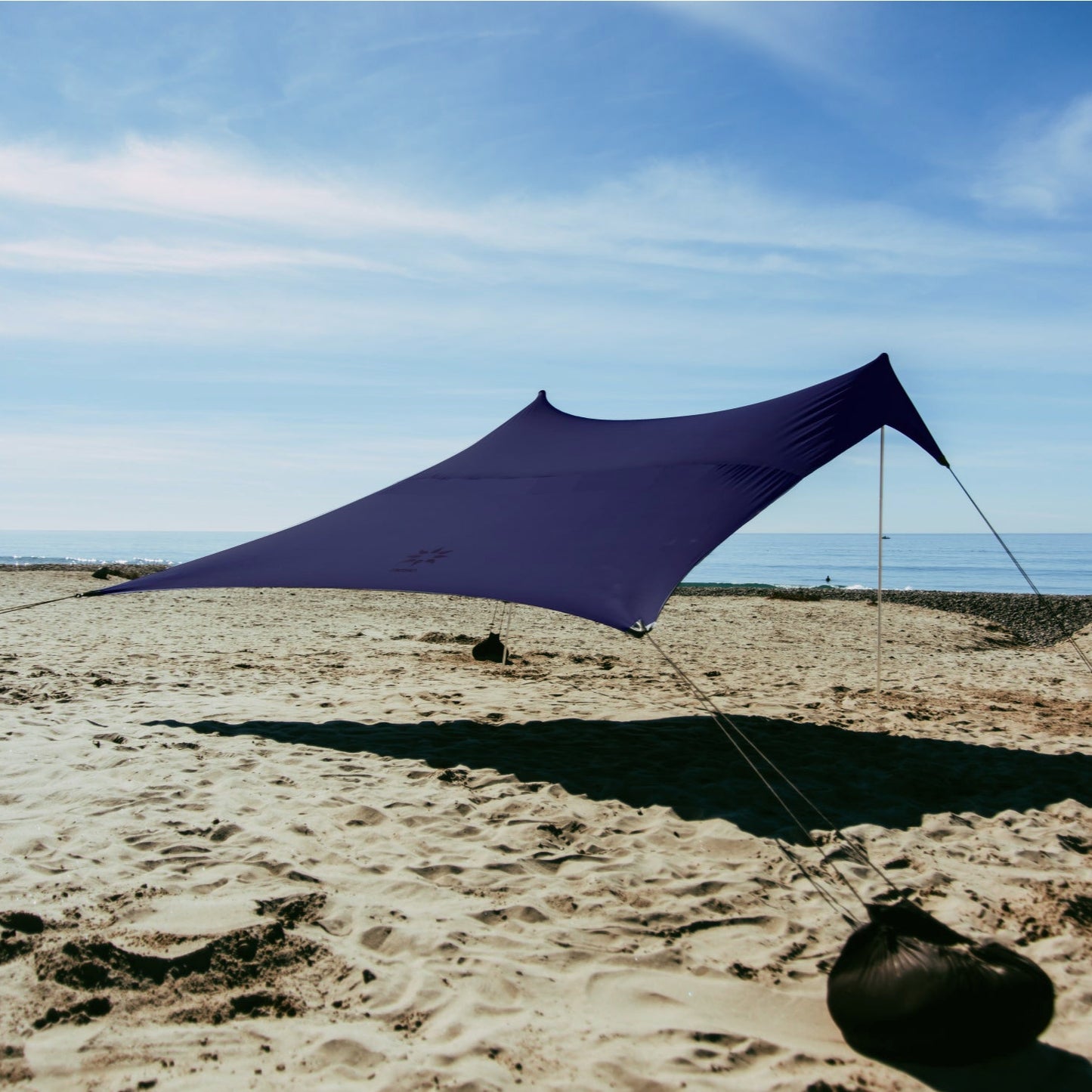 Navy NESO beach shade set up on a sandy beach with ocean in the background