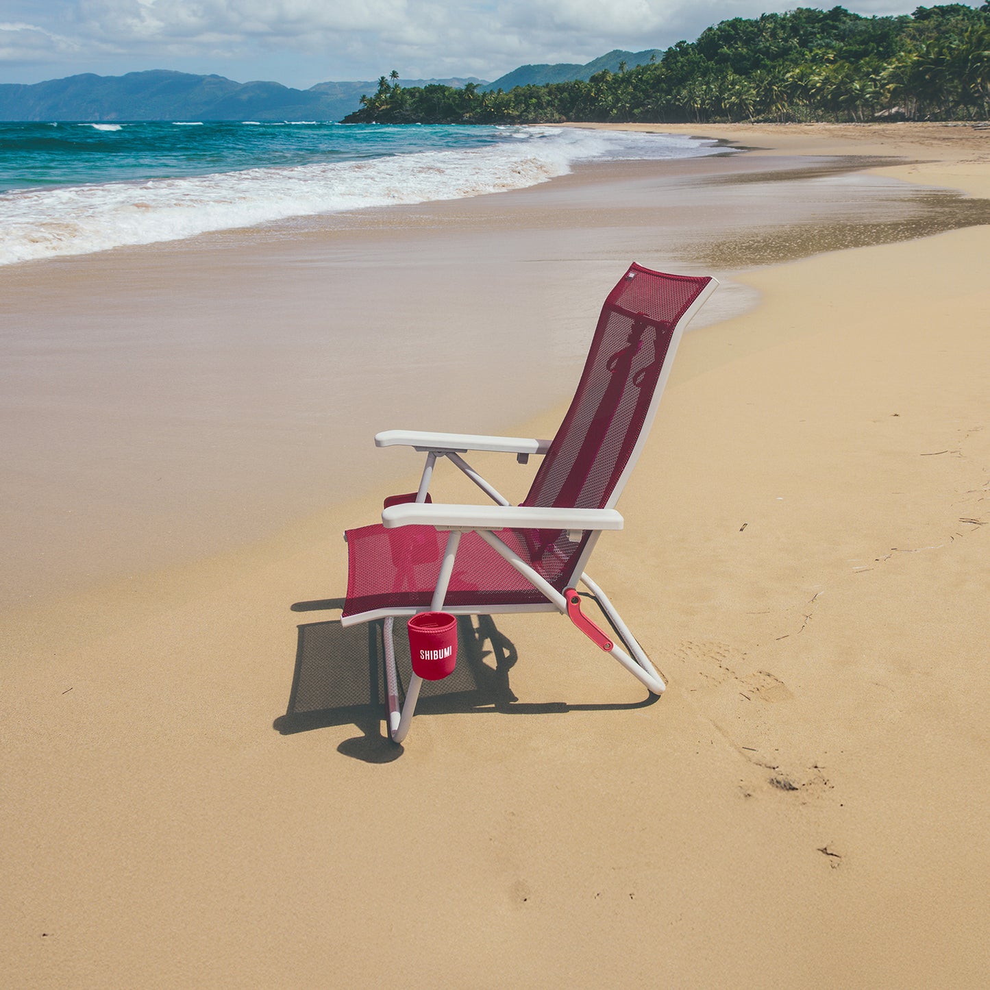 Pink and white beach chair on a sandy beach with ocean and mountains in the background