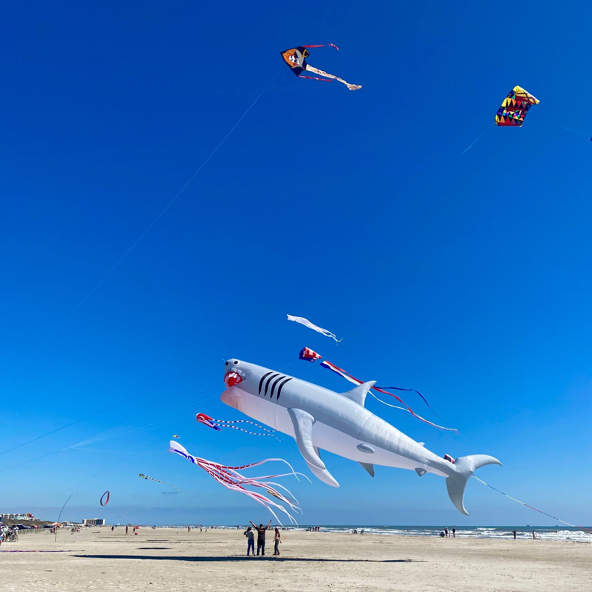 Shark-shaped kite flying over a beach with people on the sand
