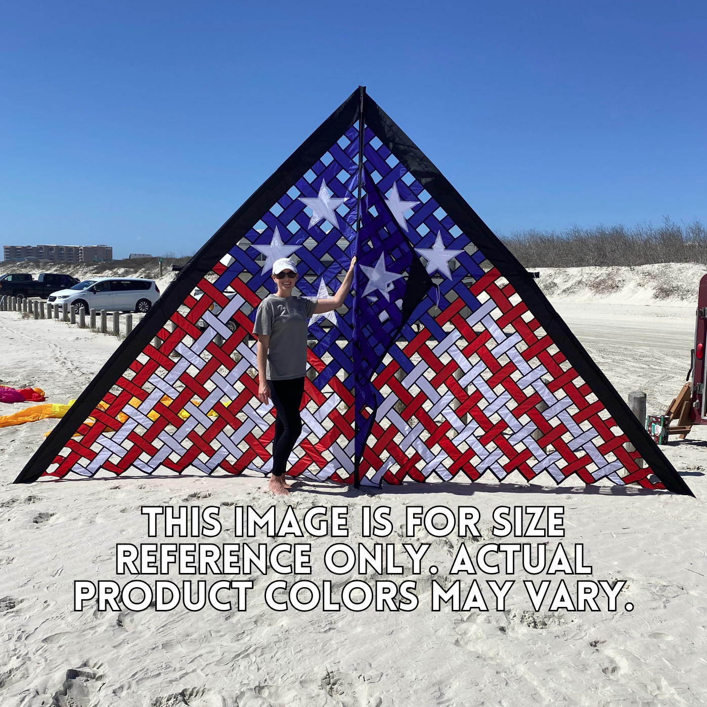 Person standing next to a large American flag kite on a sandy beach.