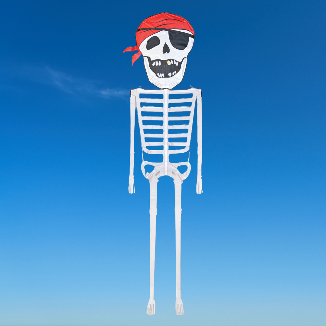 A skeleton kite with a pirate design, featuring a skull head, red bandana, and white framework, flying against a blue sky background.