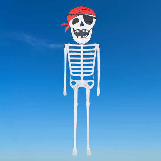 A skeleton kite with a pirate design, featuring a skull head, red bandana, and white framework, flying against a blue sky background.