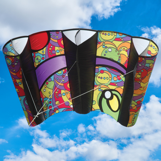 Colorful sled kite with a geometric pattern flying against a blue sky with clouds
