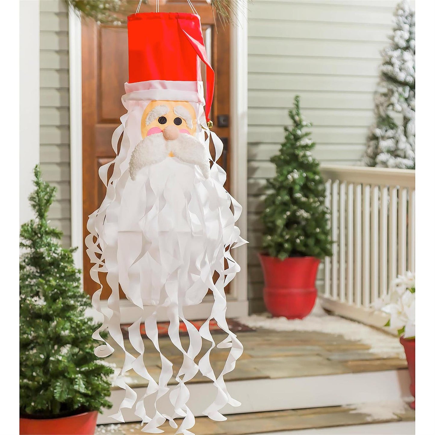 Decorative Santa Claus shaped windsock on a porch with Christmas trees and a door in the background.