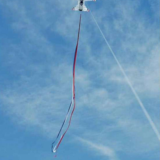 Airplane kite with a long red and white tail flying against a blue sky.
