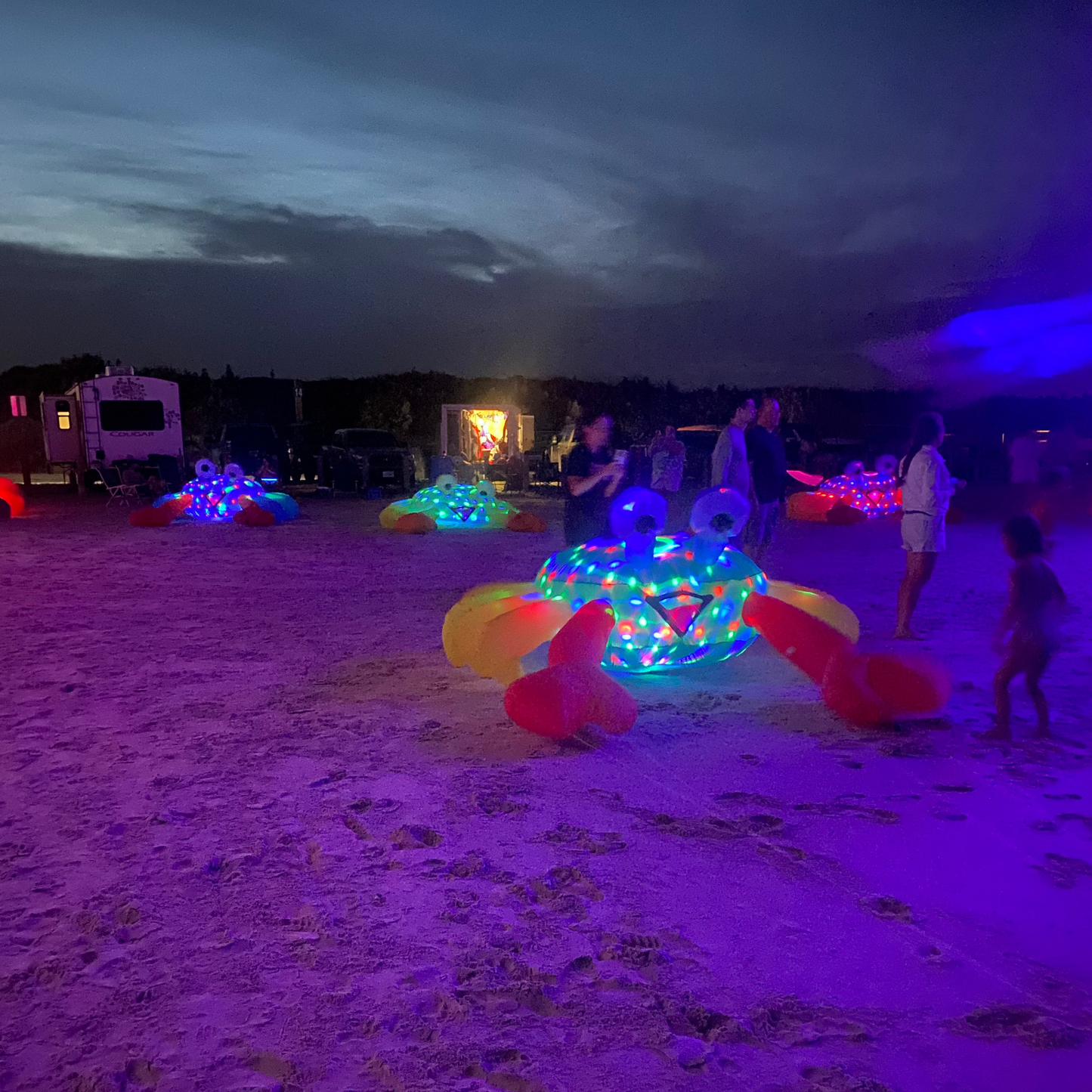 Colorful illuminated inflatable crabs on a sandy beach at night