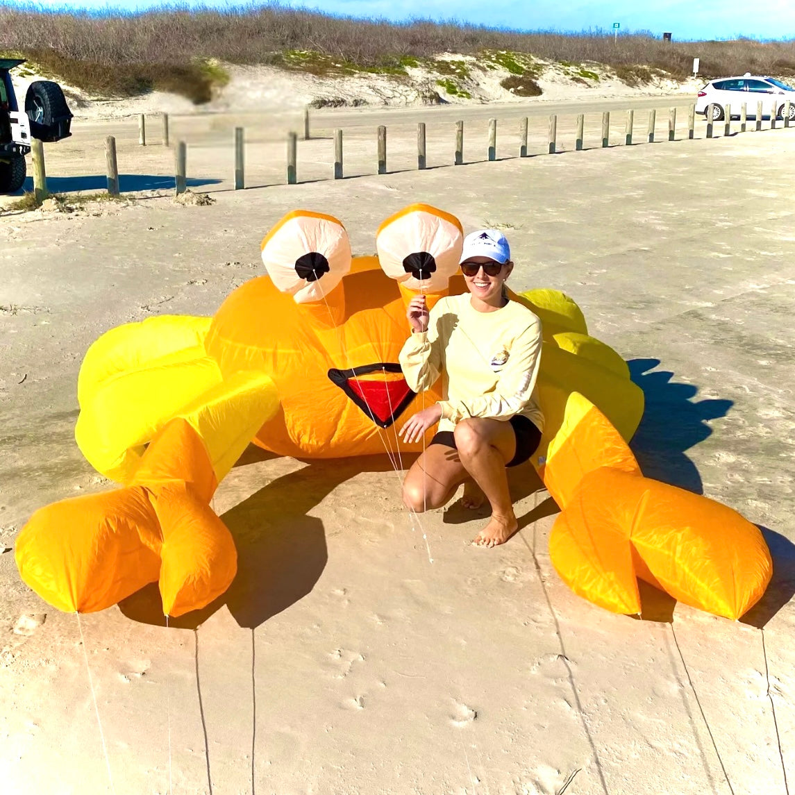 A person standing next to a large orange inflatable crab kite on a beach.