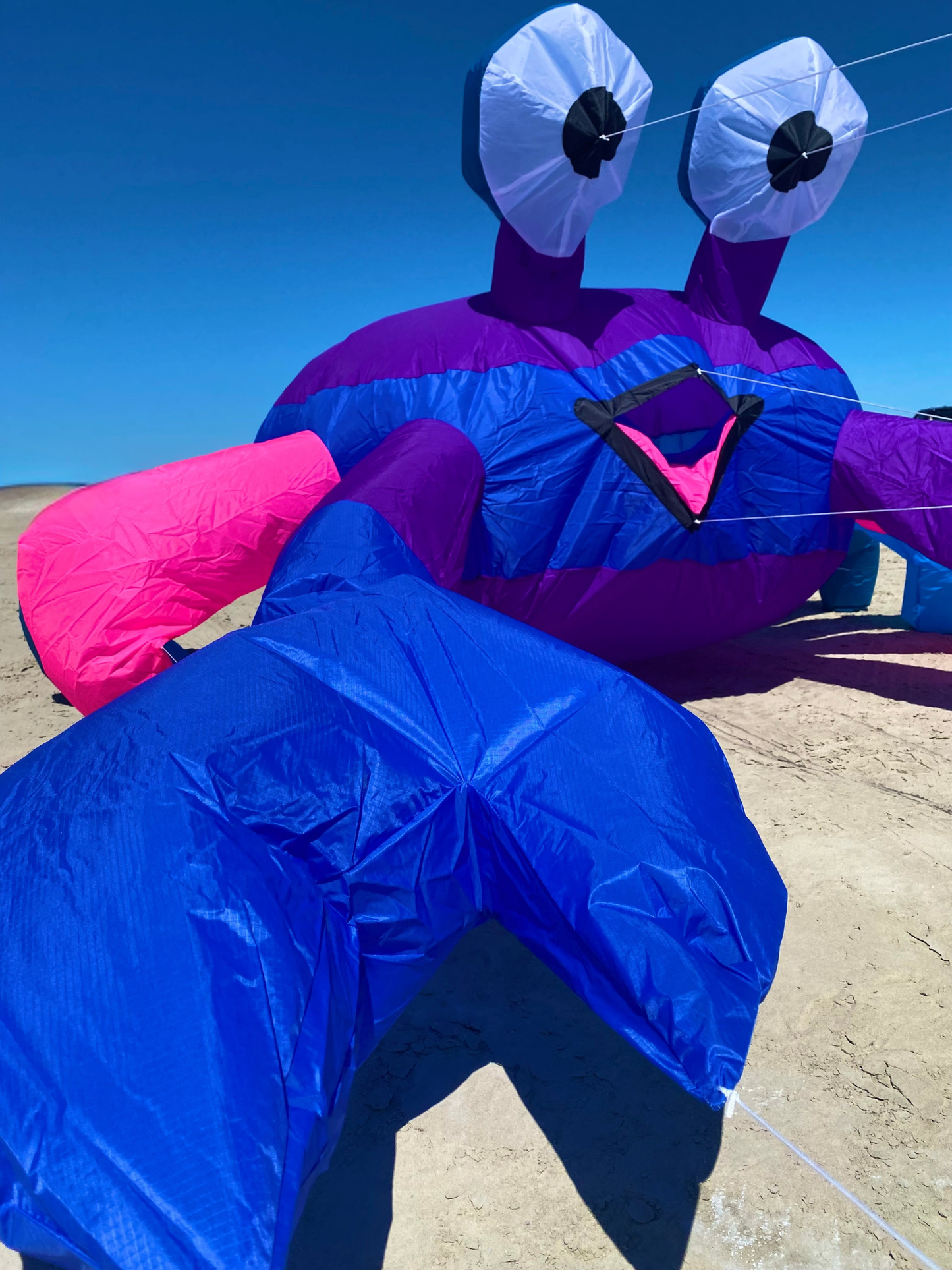 Large blue and purple kite shaped like a crab character on a clear day.