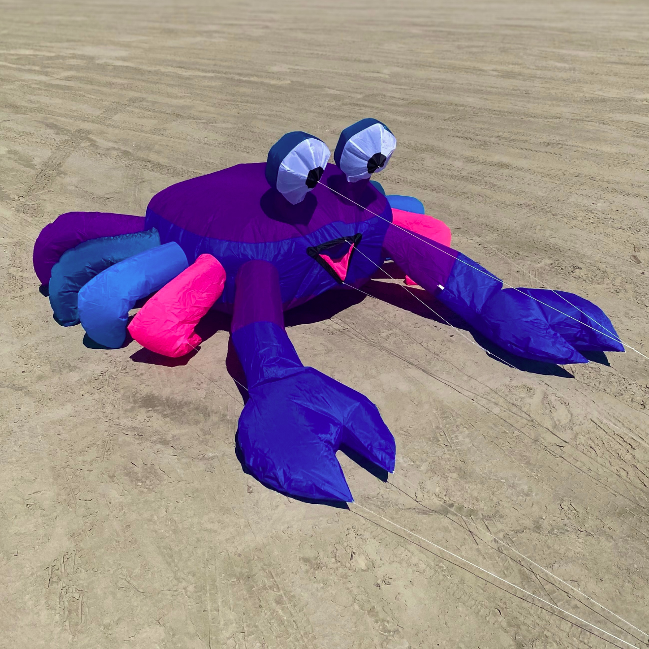 Colorful crab-shaped kite on a sandy beach with a clear blue sky.