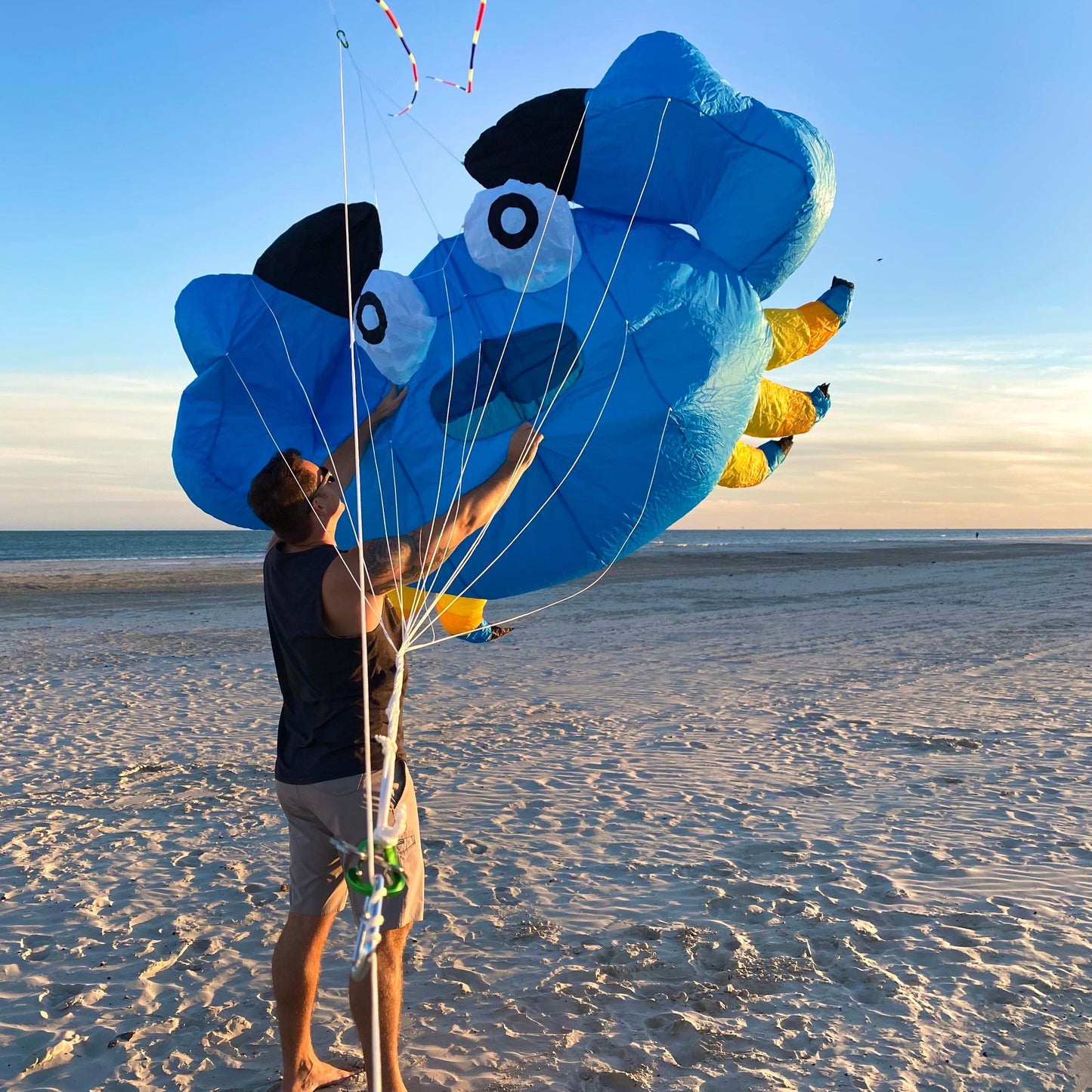 Person holding a large blue kite shaped like a crab on a sandy beach.