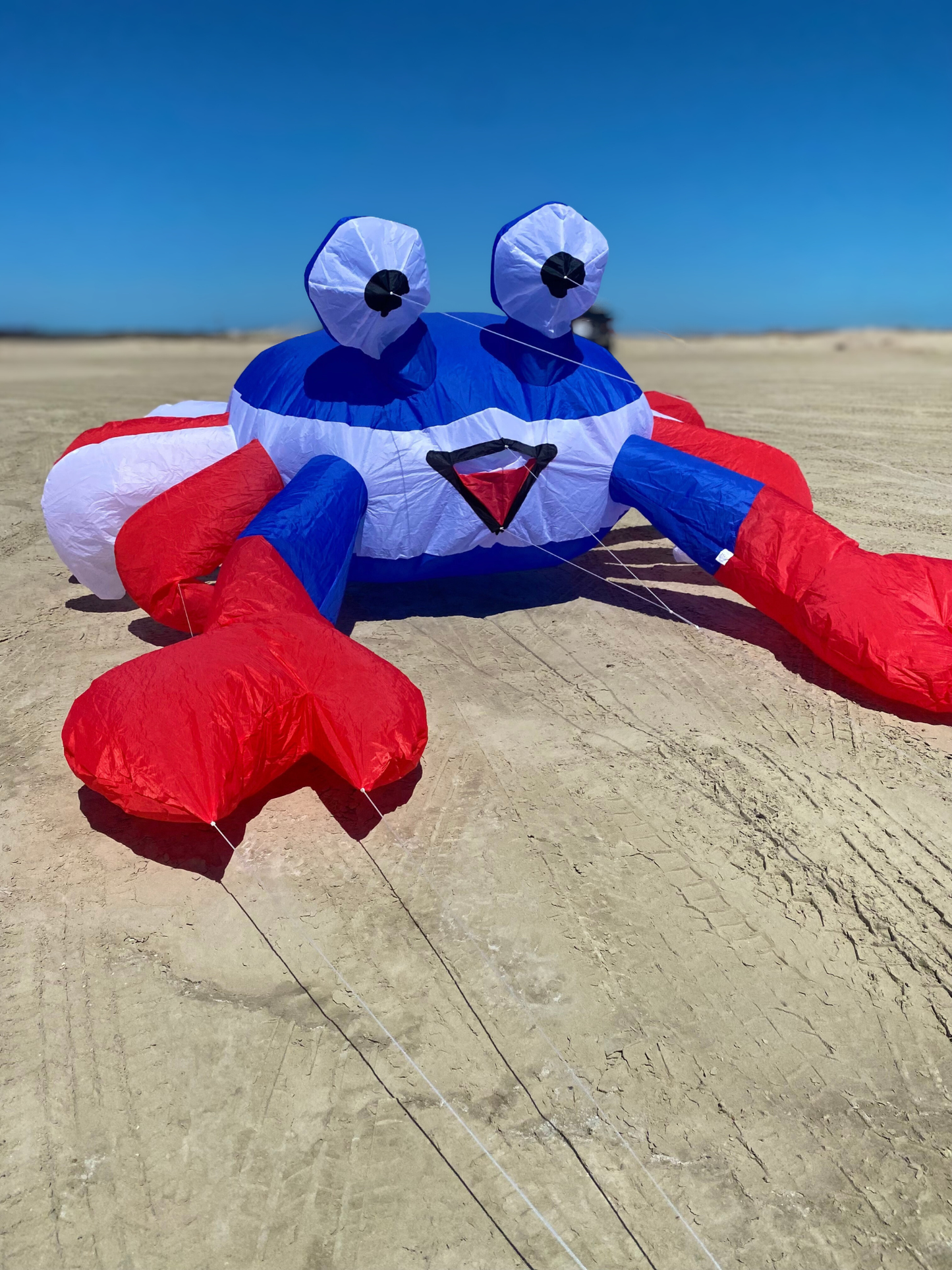 Inflatable crab kite with red, white, and blue colors on a sandy surface.