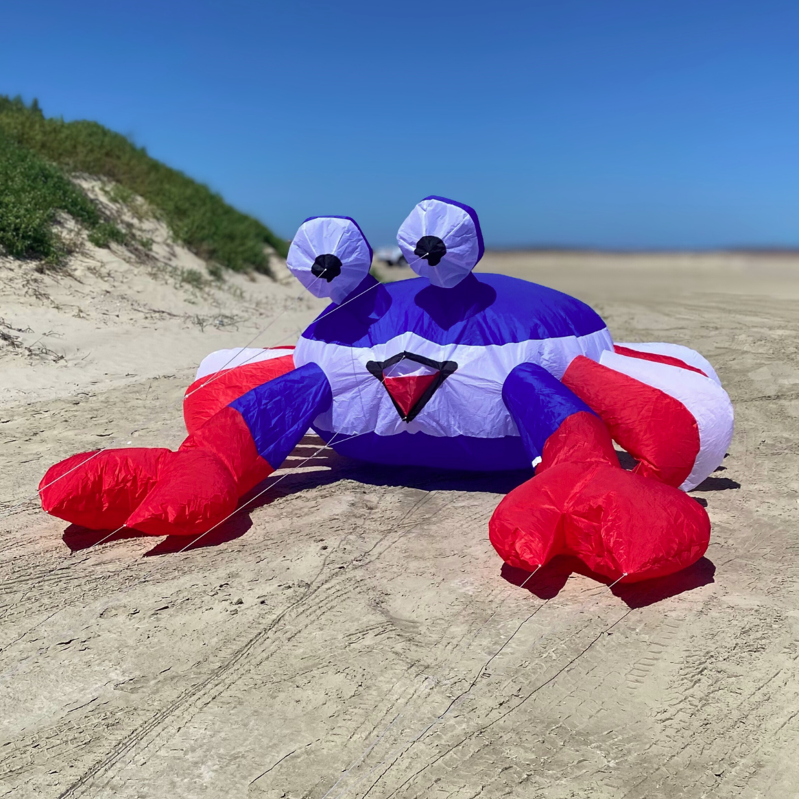Inflatable crab kite on a sandy beach with a clear blue sky.