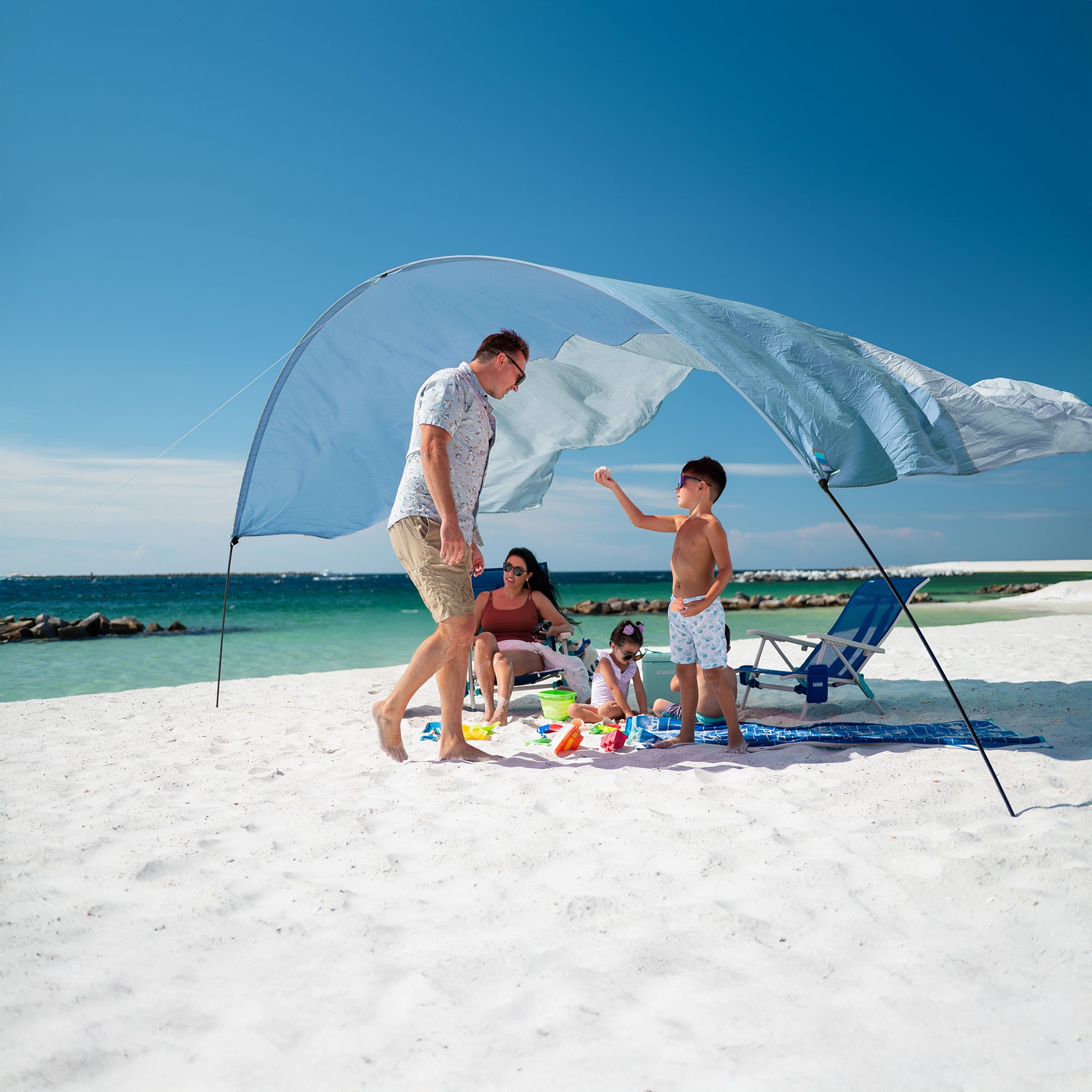 Family under a large beach shade on a sunny day at the beach.