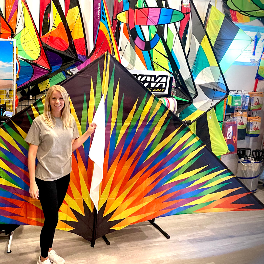 A person standing next to a large, multicolored delta kite displayed on a stand.