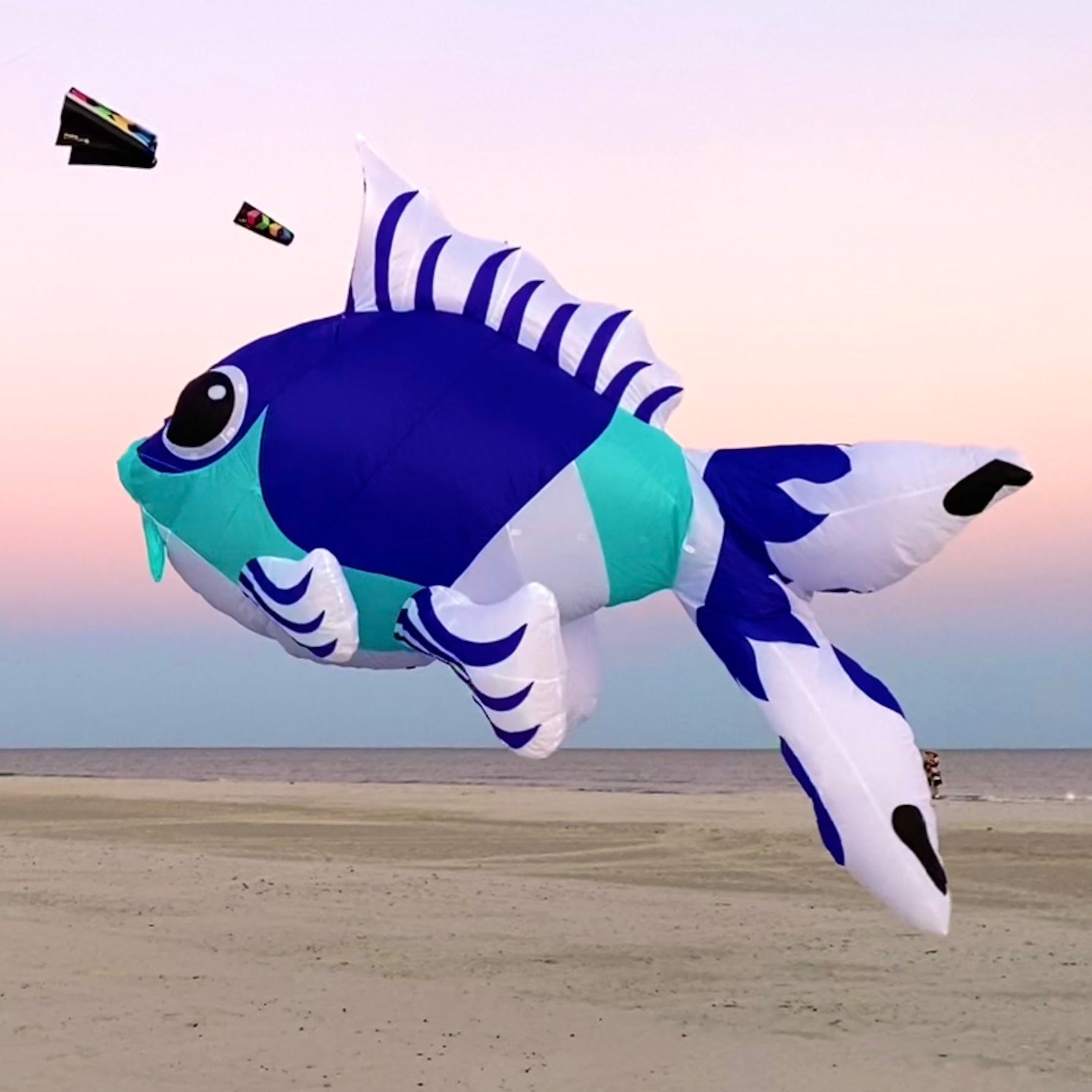 Blue and white fish-shaped kite flying over a beach with a clear sky.