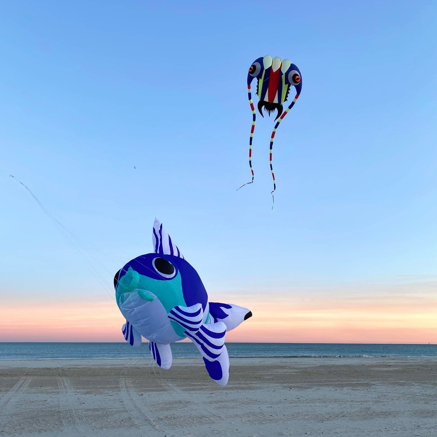 Two colorful kites flying over a sandy beach with a clear sky.