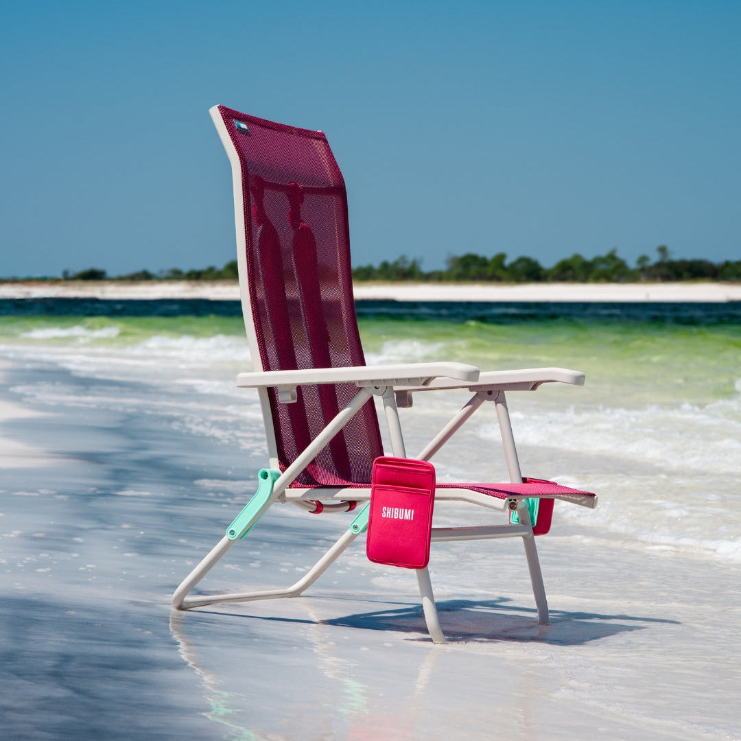 Berry color beach chair on a sandy beach with clear blue water and sky.