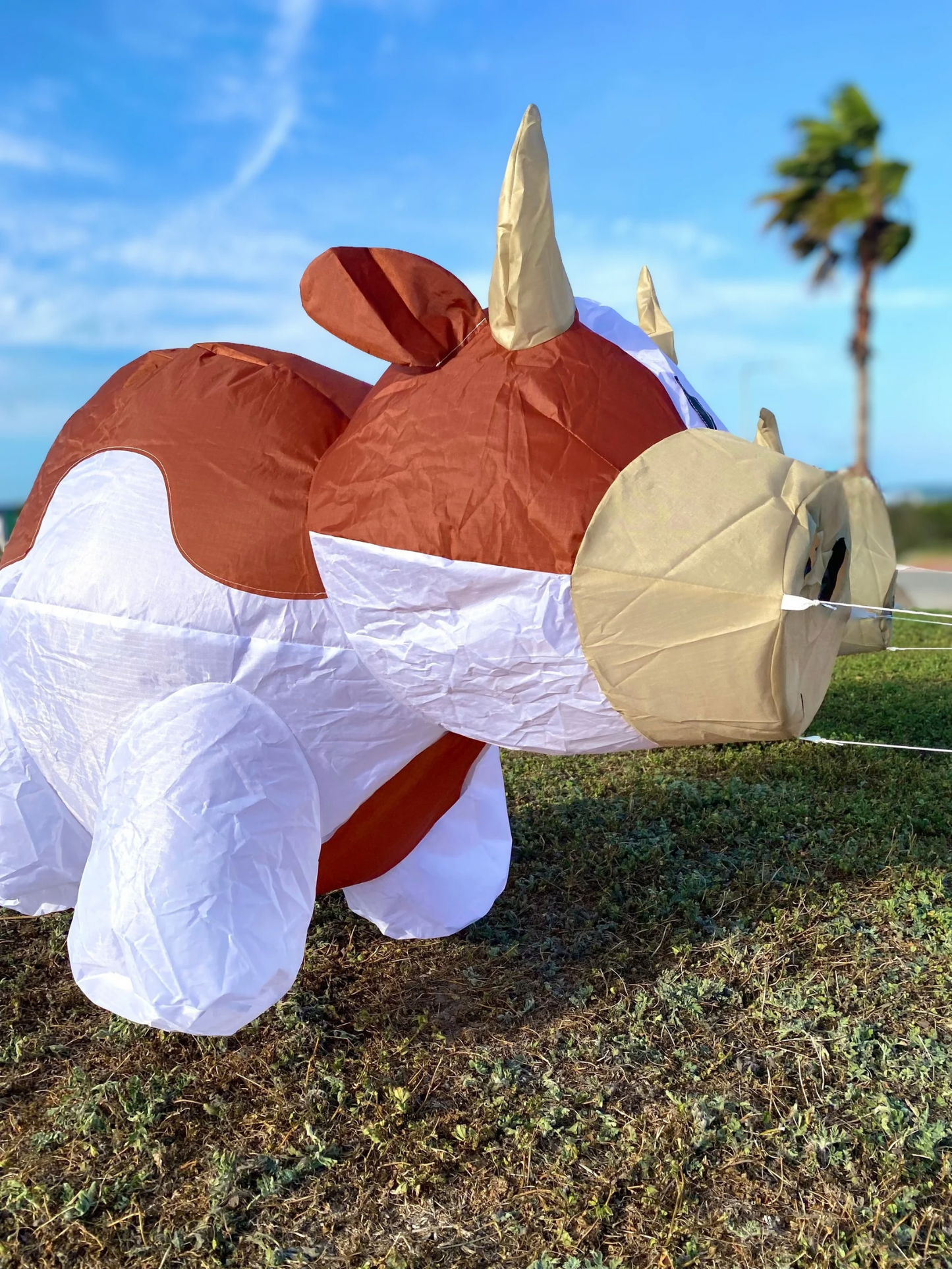 Inflatable cow character on a grassy field with palm trees in the background