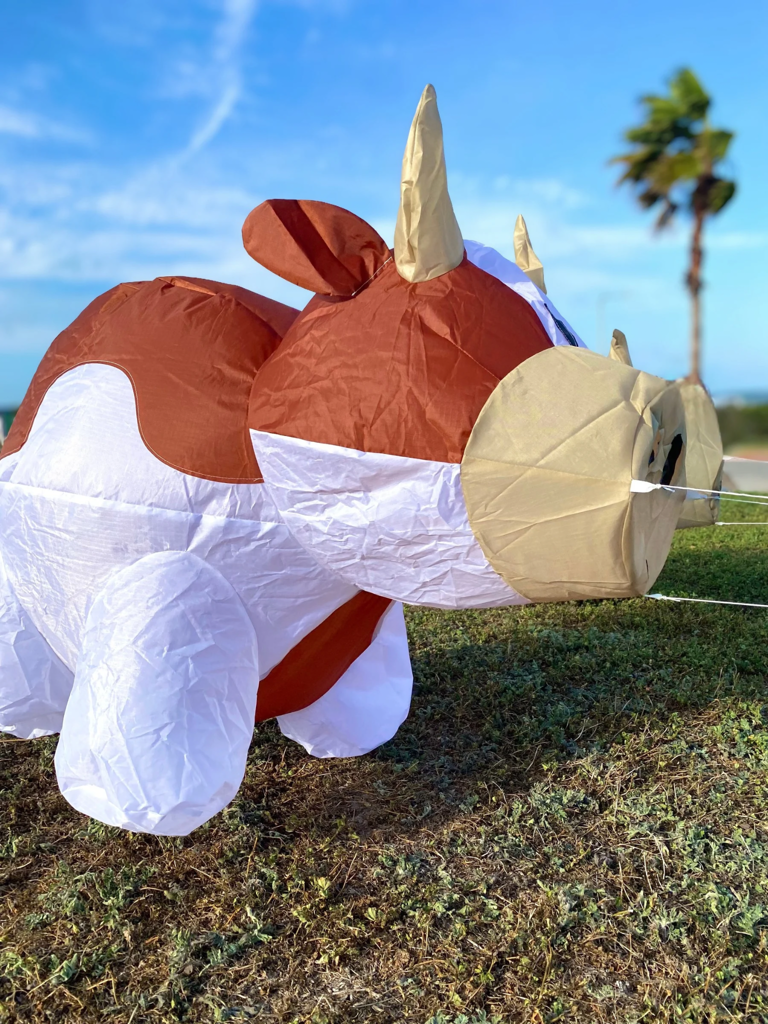 Inflatable cow character on a grassy field with palm trees in the background