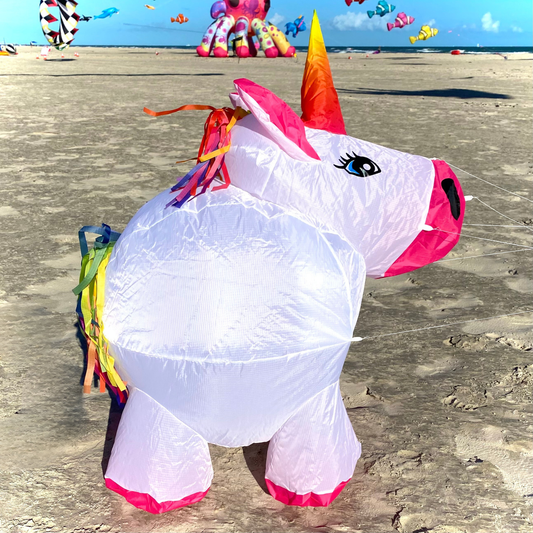 Colorful unicorn kite on a sandy beach with other kites in the background.