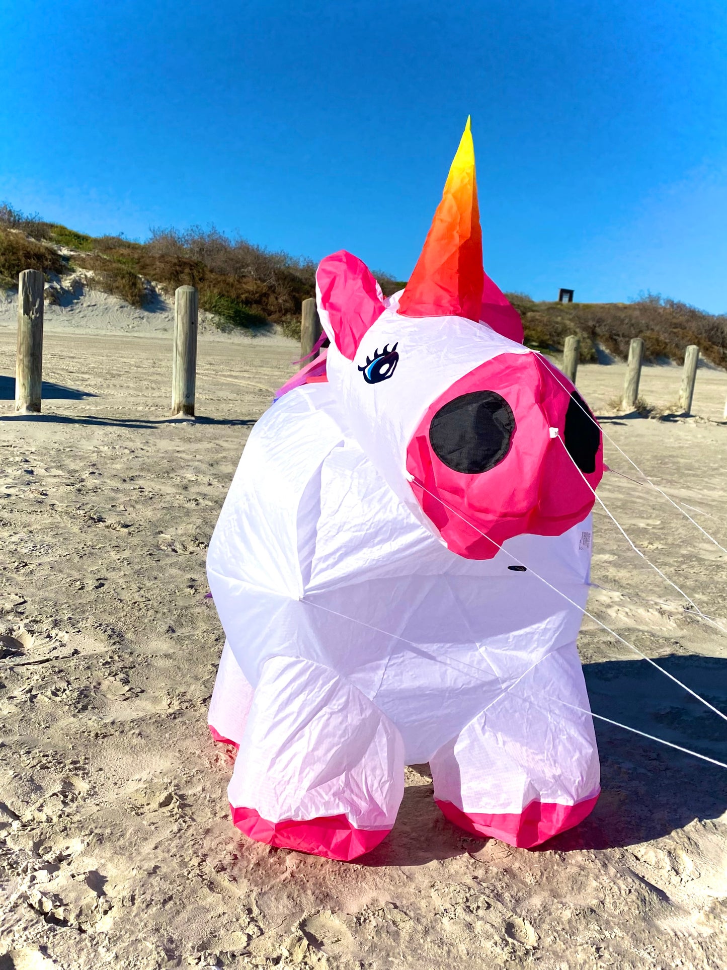 Inflatable unicorn kite on a sandy ground with a clear blue sky