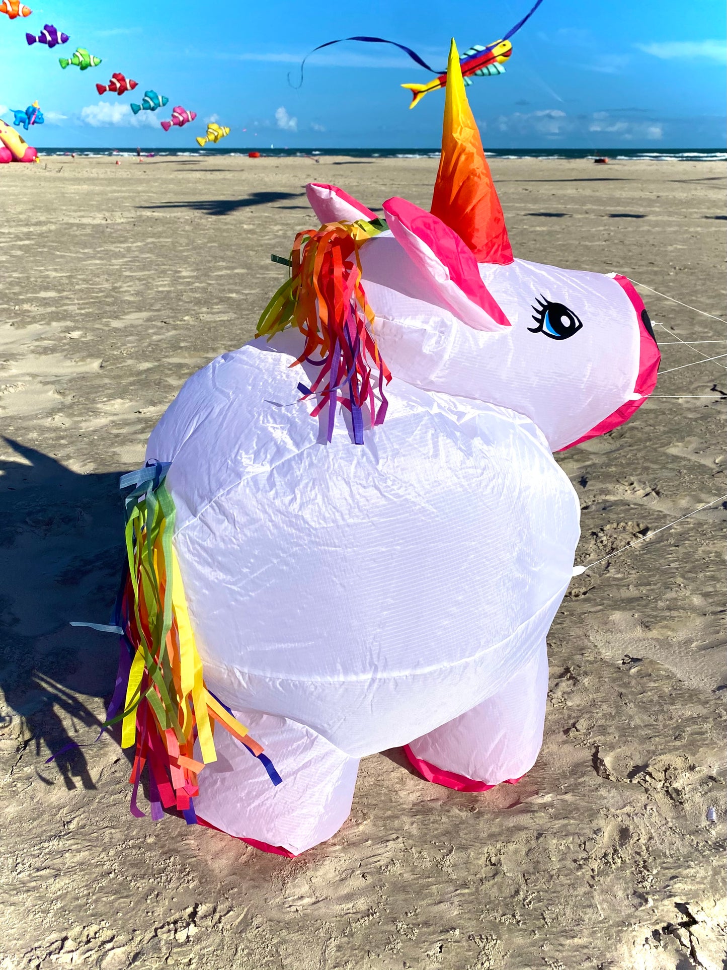 Unicorn-shaped kite on a sandy beach with ocean and sky in the background