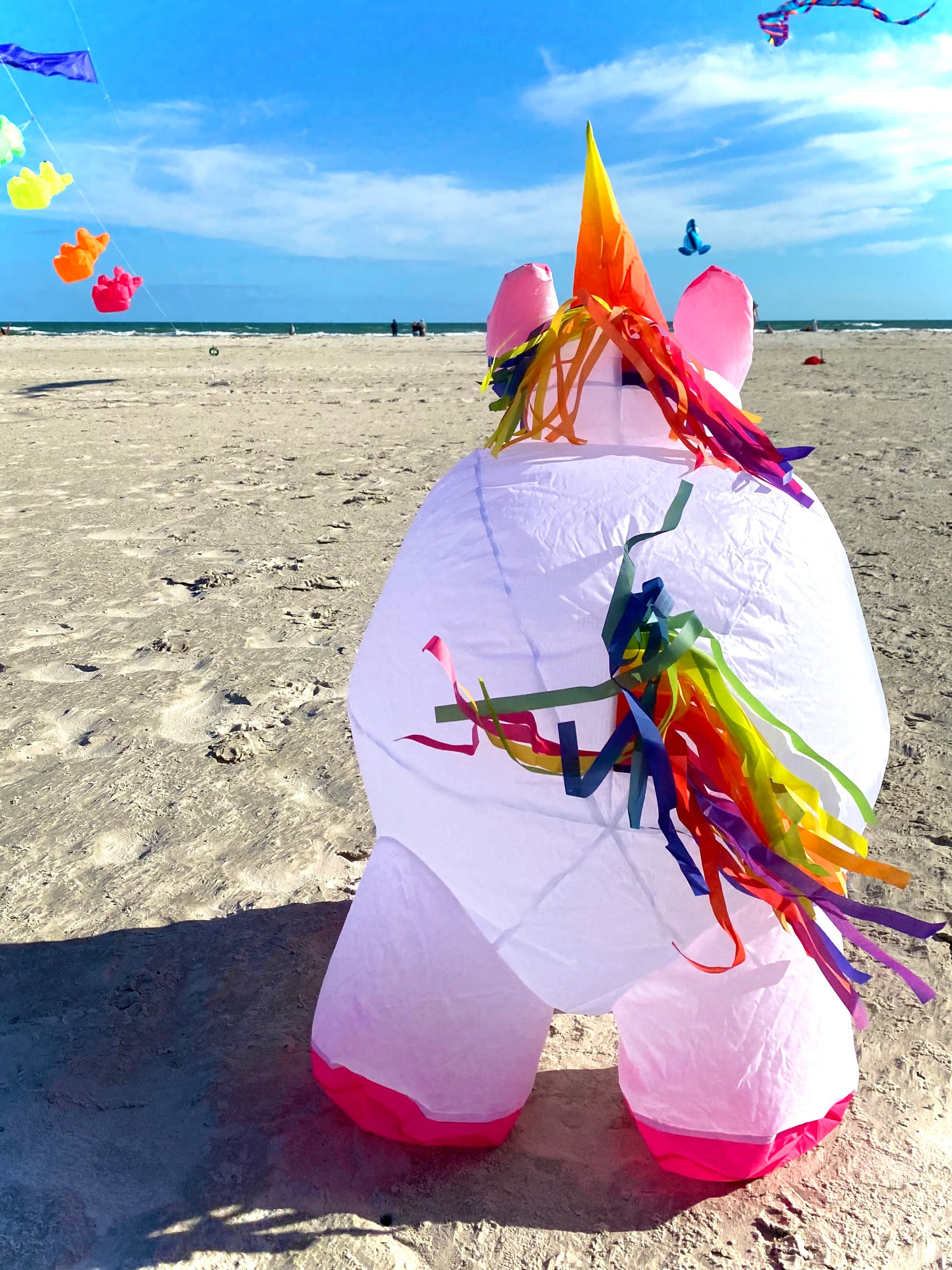 Inflatable unicorn kite on a sandy beach with colorful streamer tail and mane. 