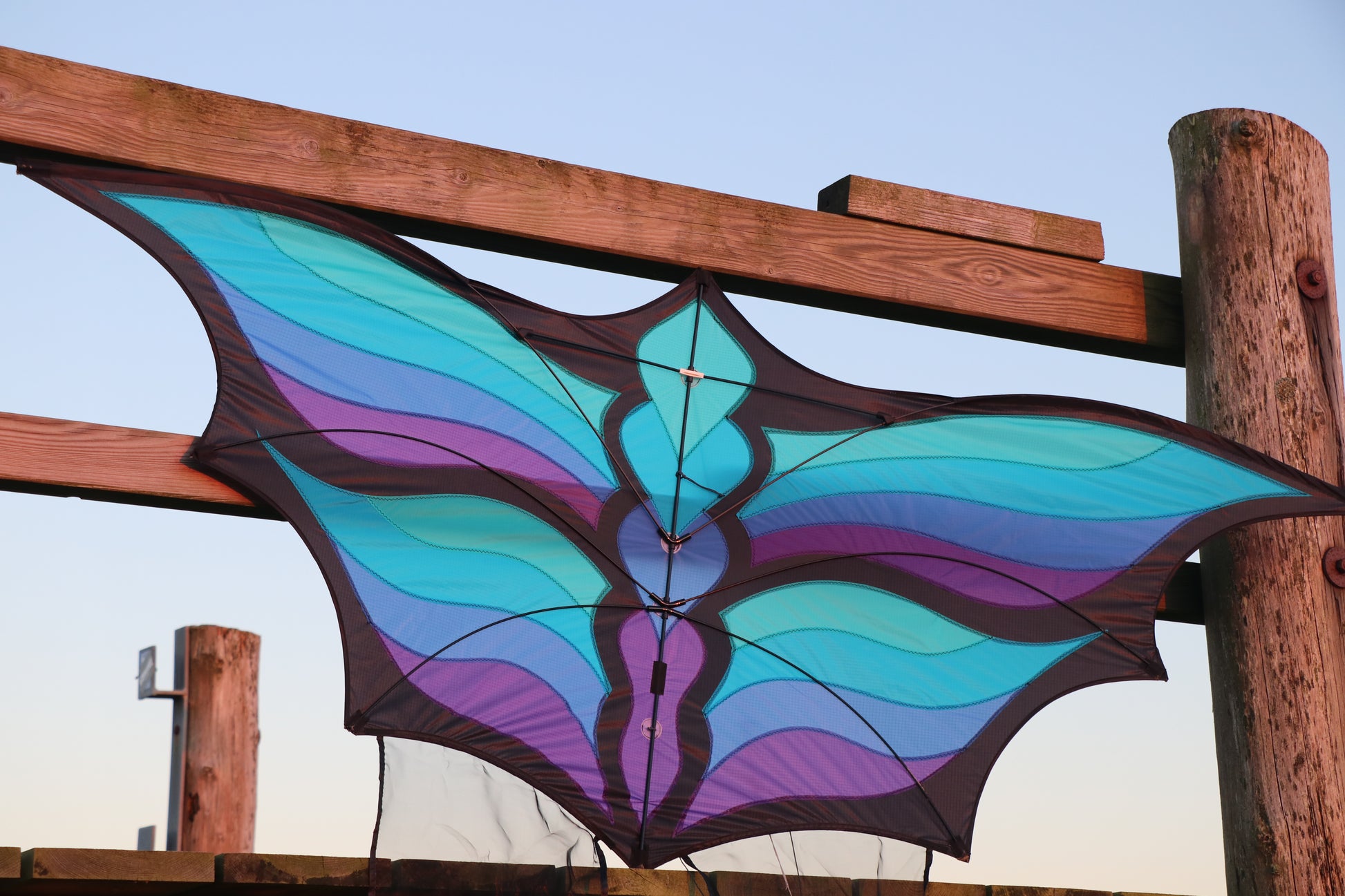 Colorful butterfly-shaped kite against a wooden fence and blue sky.