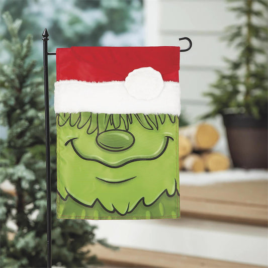 Decorative garden flag with a green face design on a black pole outdoors.