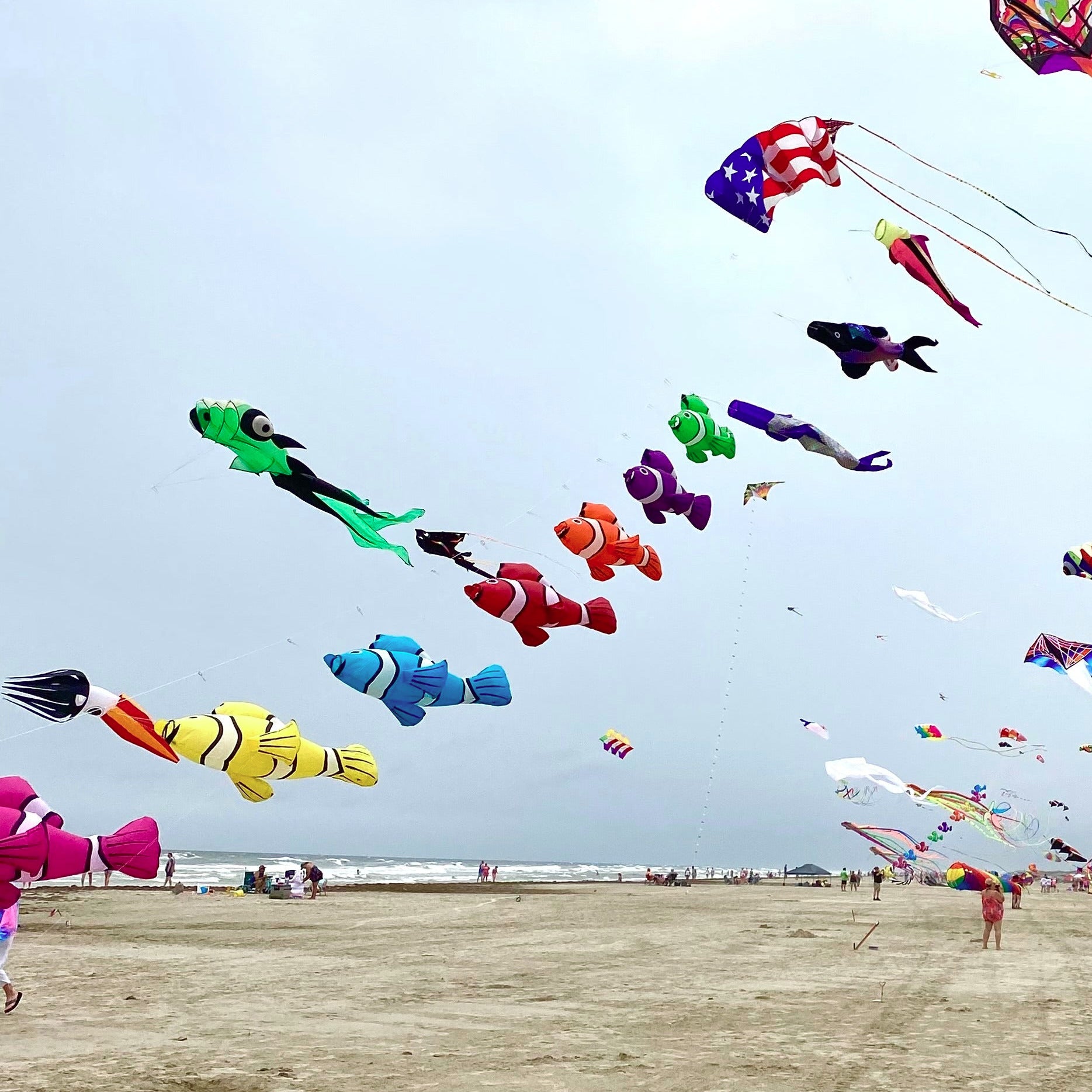 Colorful kites flying over a sandy beach with people below.