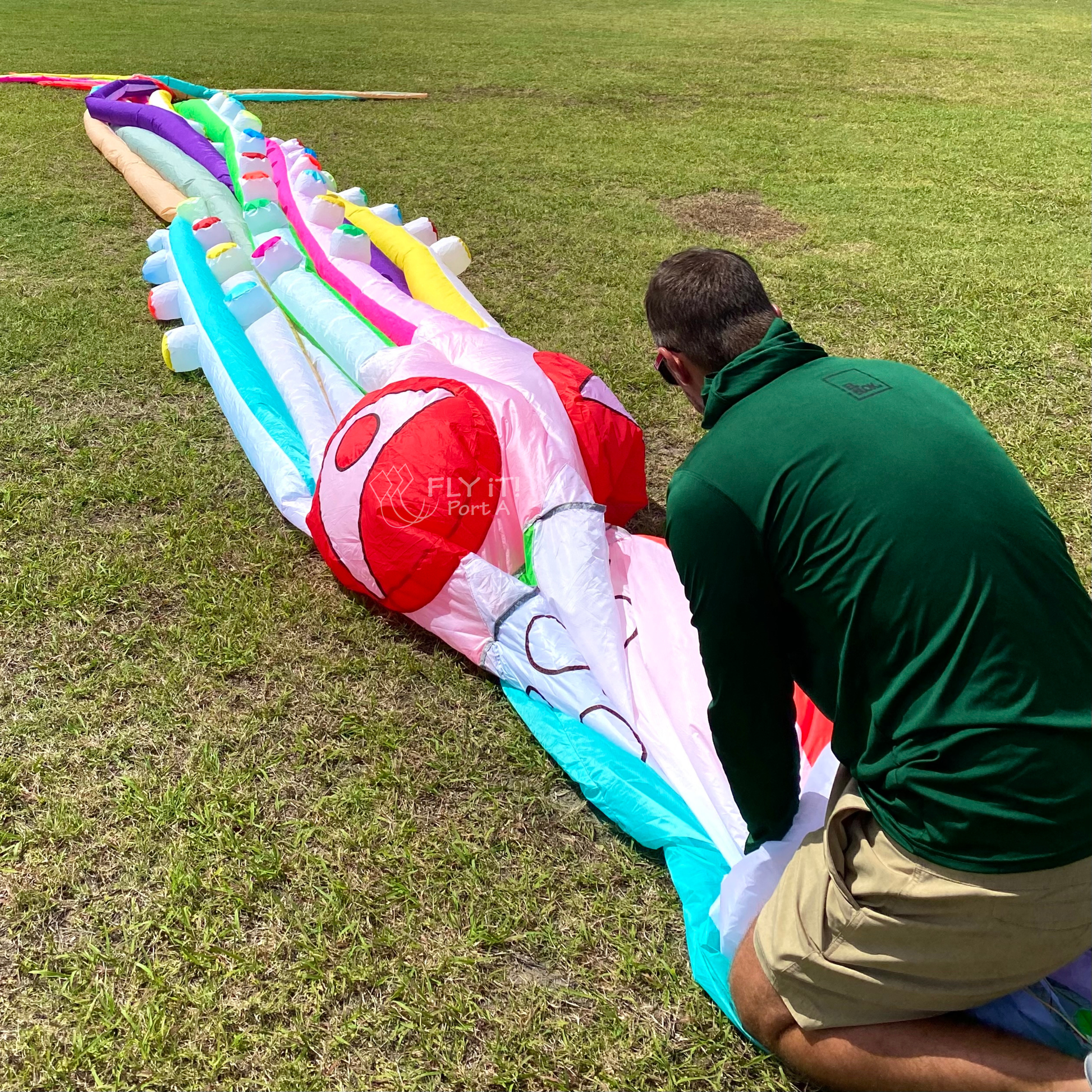 Man working on a large, colorful inflatable kite on a grassy field