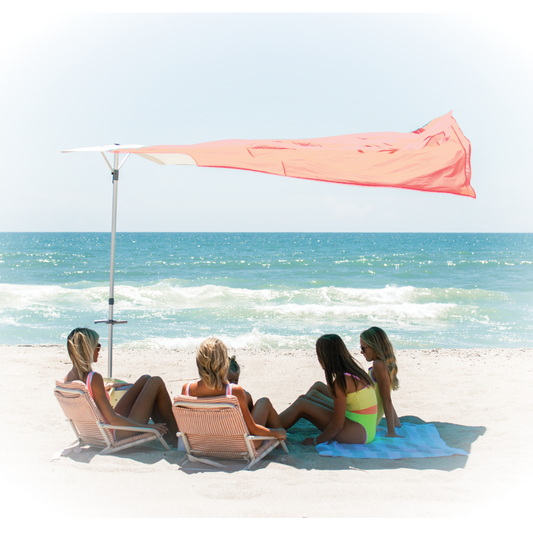 Four women sitting on beach chairs under a coral colored canopy with ocean view