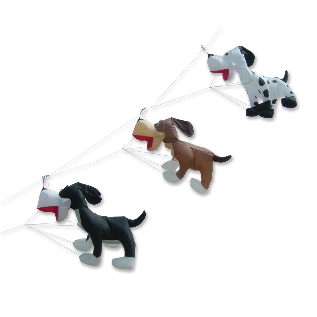 Three hanging dog-shaped kites in black, brown, and white with red and beige details, suspended by thin strings against a plain white background