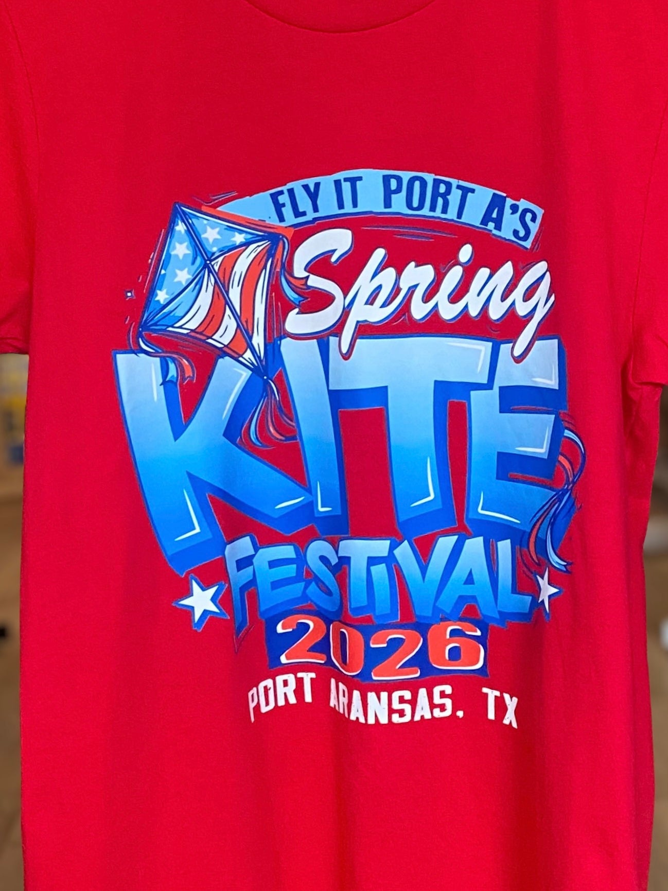 Red t-shirt with 'Spring Kite Festival 2026' graphic design on a blurred background