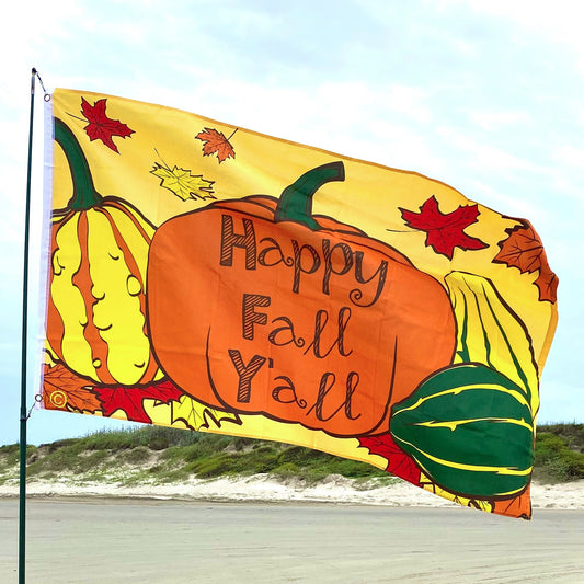 Colorful 'Happy Fall Y'all' flag with pumpkins and leaves on a beach.
