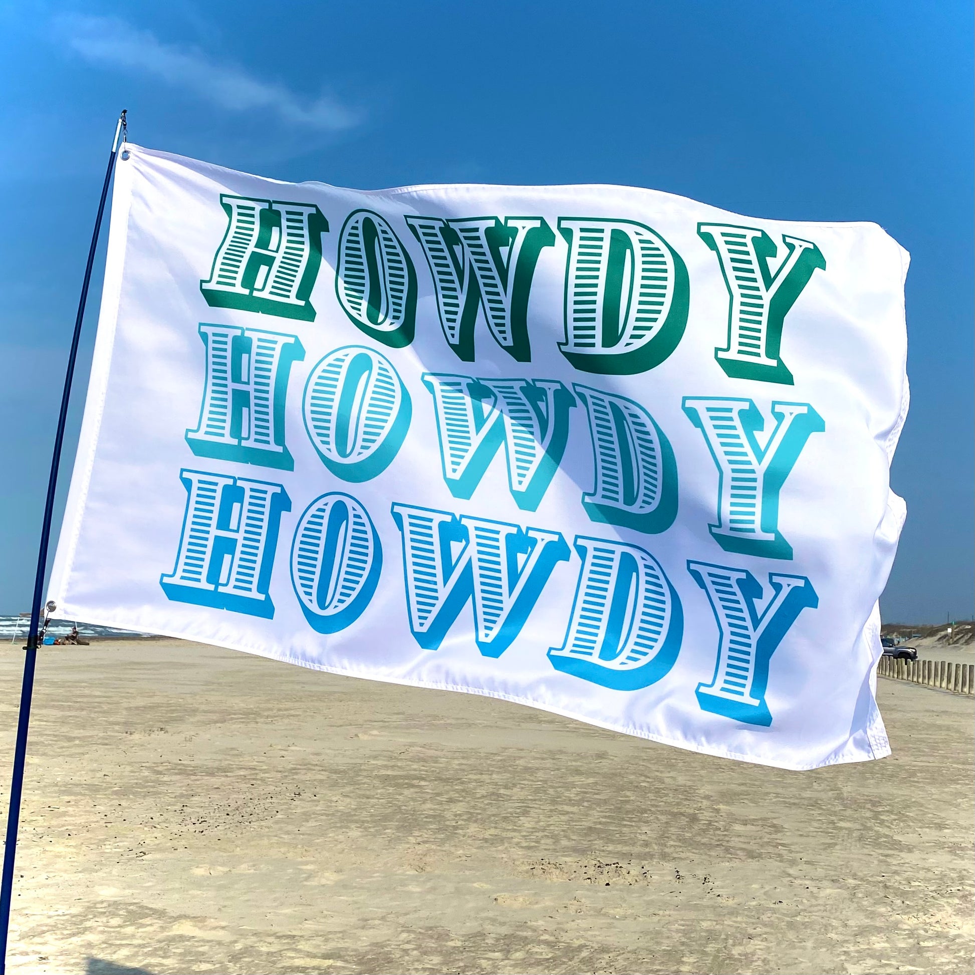 White flag with 'HOWDY' text in green and blue on a beach.