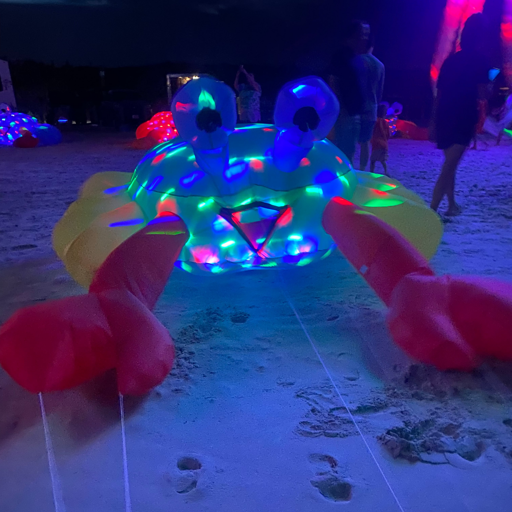 Colorful LED inflatable crab on a sandy surface with people in the background