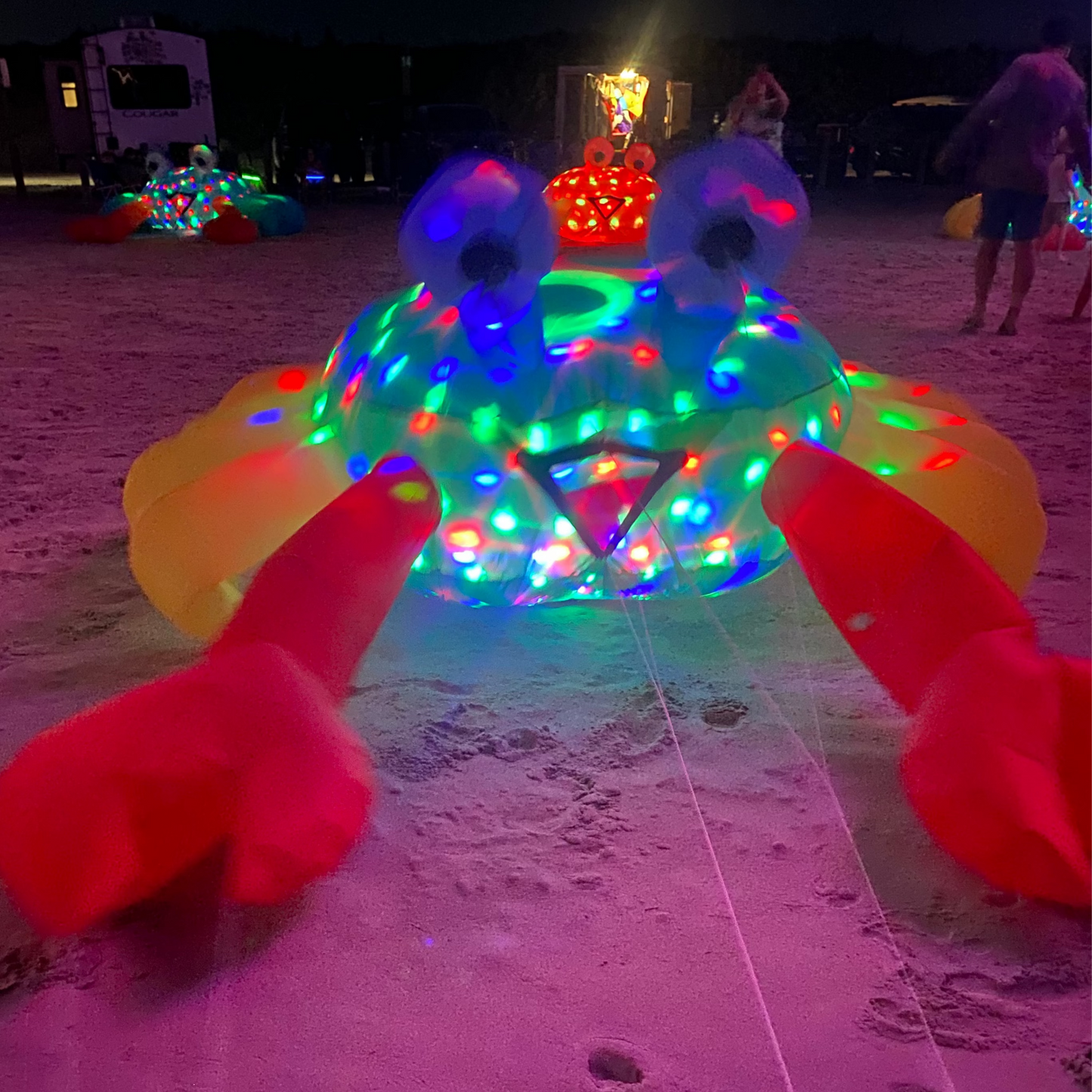 Inflatable crab with colorful lights on a sandy beach at night